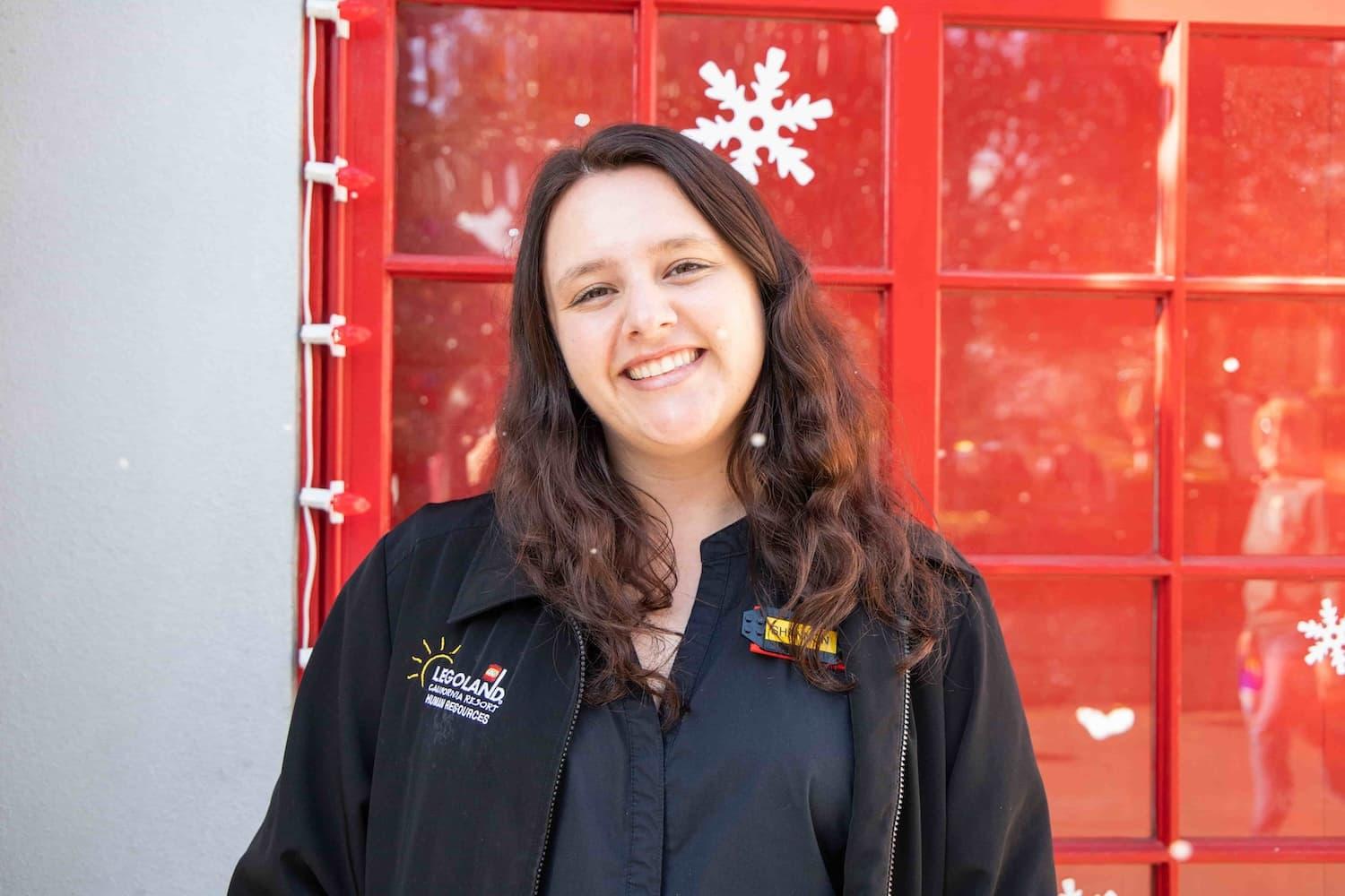 Headshot of a female LEGOLAND employee smiling directly into the camera. She has a LEGOLAND jumper on with a name badge on her chest.