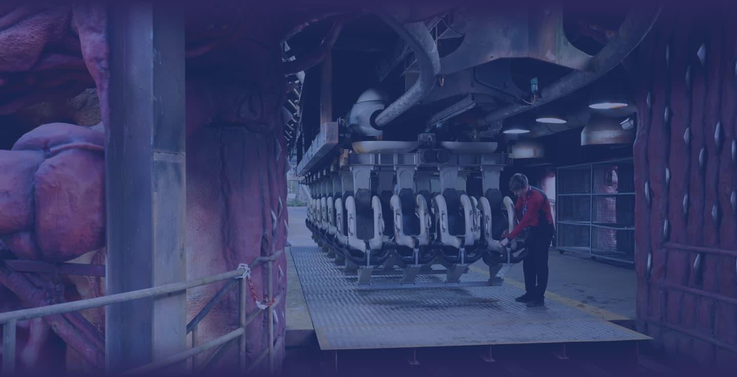 A staff member in red maintains an empty attraction ride at a Thorpe Park. The walls are purple.